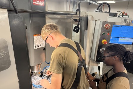 在弗吉尼亚州李堡，陆军中士沙恩·格莱姆斯指导列兵查丽蒂·德拉格和二等兵埃文·夏普如何在数控铣床上验证切割长度和宽度是否符合图纸