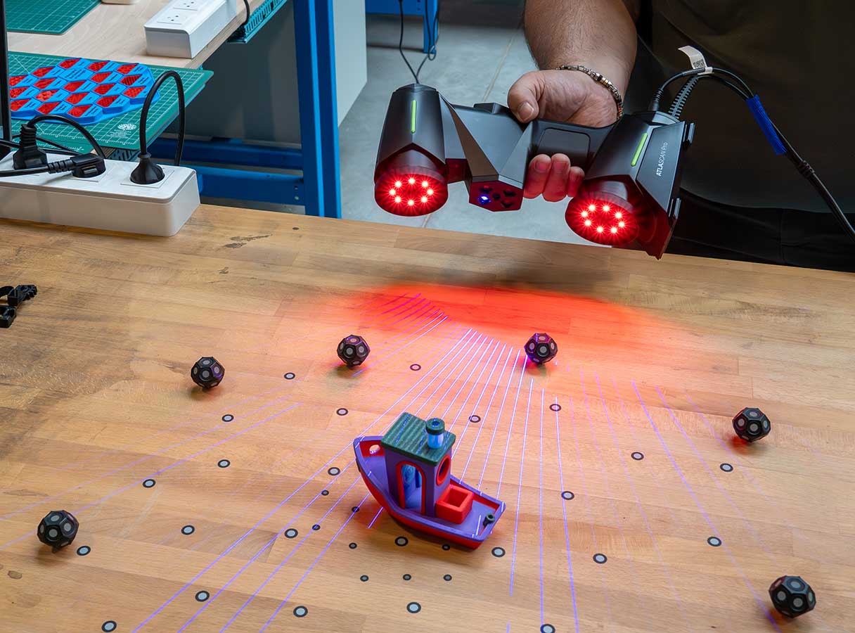 用户正在操作 Hexagon 的 ATLASCAN Pro 手持式 3D 扫描仪，在工作台上扫描 3D 打印的 Benchy 模型几何形状